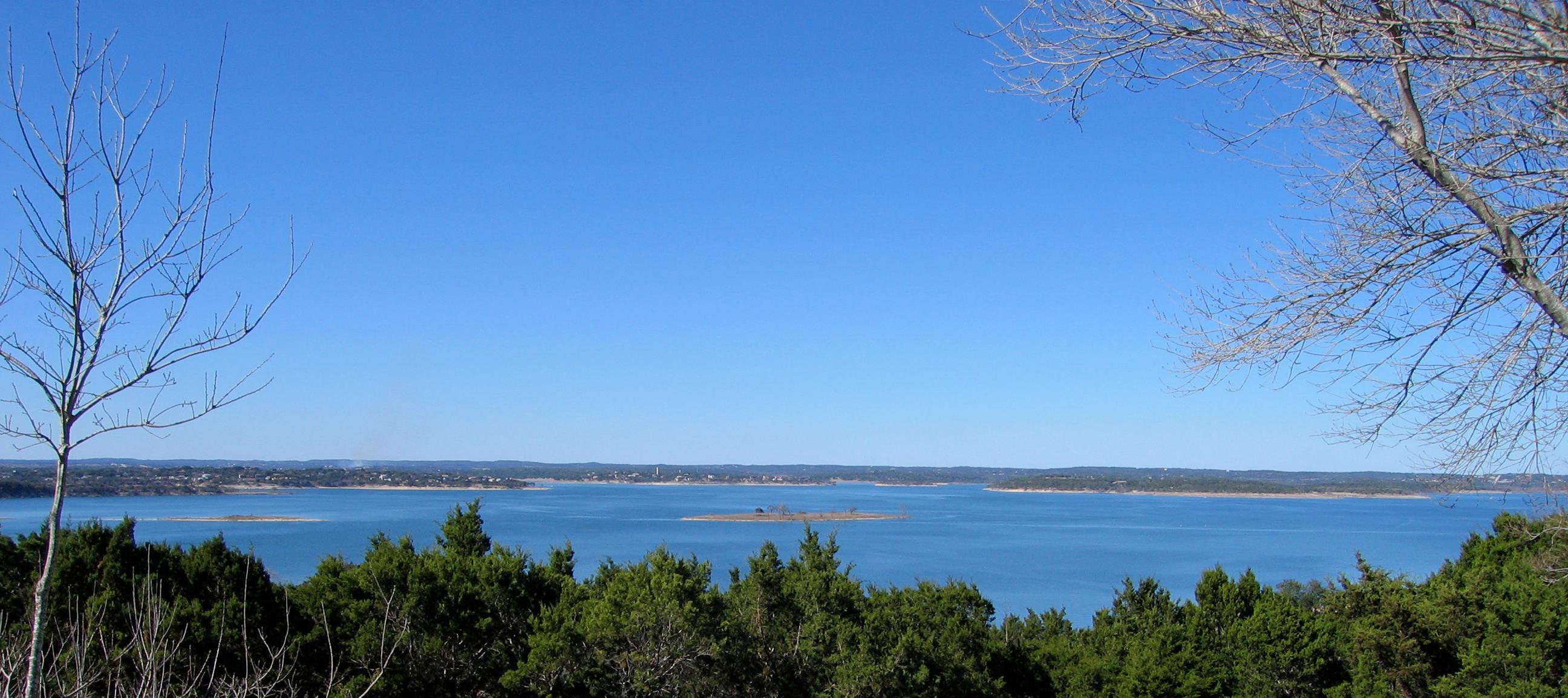 A wide view of Canyon Lake from wooded hills above, with small islands and a distant shoreline